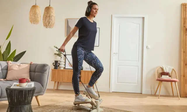 Une femme fait du step à la maison, casque sur les oreilles, pour un entraînement cardio efficace dans son salon.