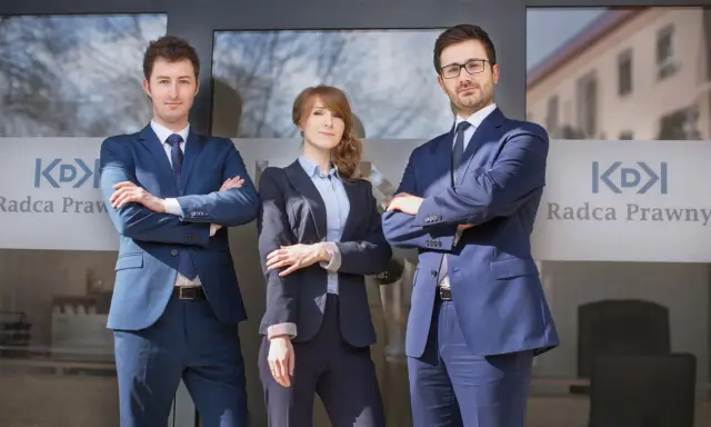 Trzech prawników w garniturach stoi przed budynkiem z logo "Radca Prawny".