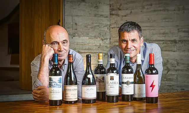 Dos hombres sonríen detrás de una fila de botellas de vino. Uno de ellos es el dueño de Bodegas Olarra.