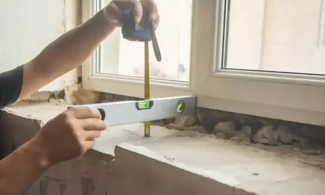 Ręce mierzą taśmą i poziomują, by wiedzieć, jak zmierzyć parapet wewnętrzny.