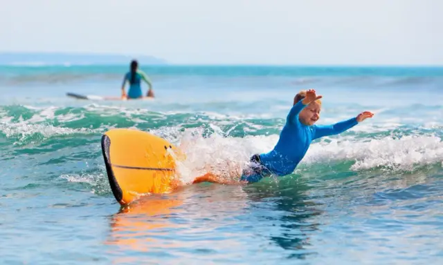 Niño sonriente surfeando en Portugal, una actividad genial que ver en Portugal con niños.