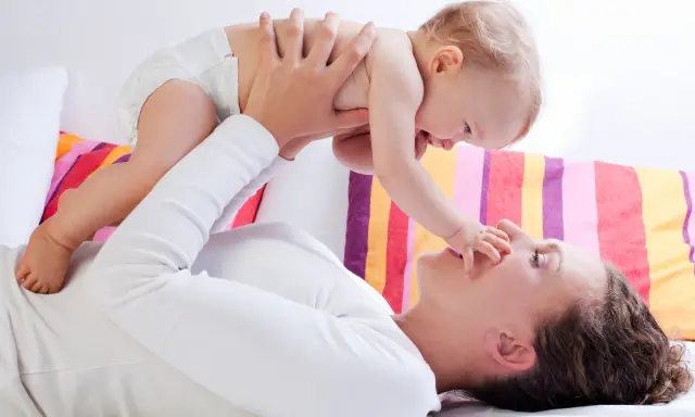 Mama podnosi dziecko, które wyciąga rączkę do jej nosa. Zdjęcie symbolizuje troskę o rozwój malucha, jak omega 3 dla niemowląt.