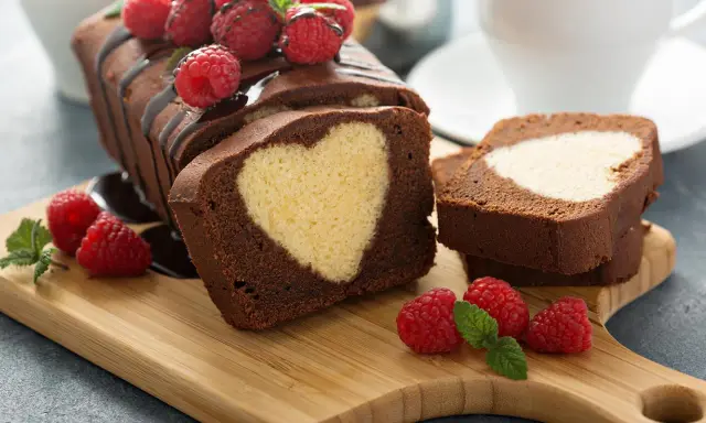 Schokoladen-Kastenkuchen mit einem hellen Herz im Inneren, garniert mit frischen Himbeeren und Schokoladensauce.