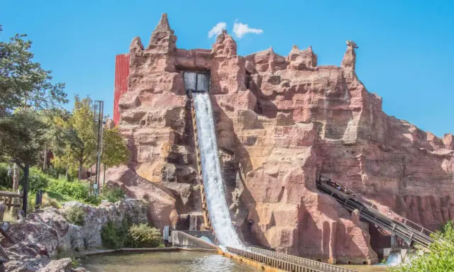 Aventura acuática en uno de los parques de atracciones en España. Un tronco desciende por una cascada artificial en un paisaje rocoso.