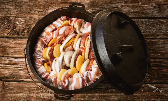 Dutch oven mit Fleisch, Kartoffeln und Zwiebeln, bereit für köstliche Dutch Oven Rezepte auf dem Gasgrill.