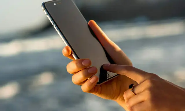 Dłoń trzyma iPhone 13, który nie chce się włączyć. Palec wskazujący próbuje go ożywić.