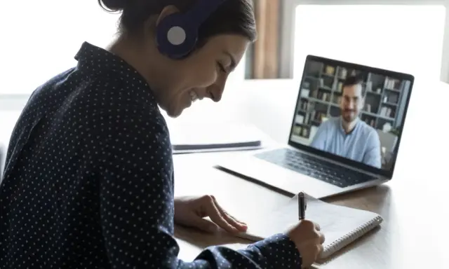Ragazza con cuffie sorride mentre prende appunti durante una lezione online, comprendendo il vero e-learning significato.