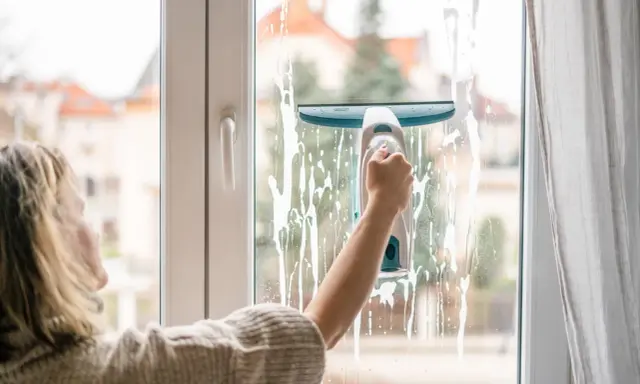 Kobieta myje okno elektrycznym odkurzaczem do szyb, by dowiedzieć się, jak myć okna żeby nie było smug.
