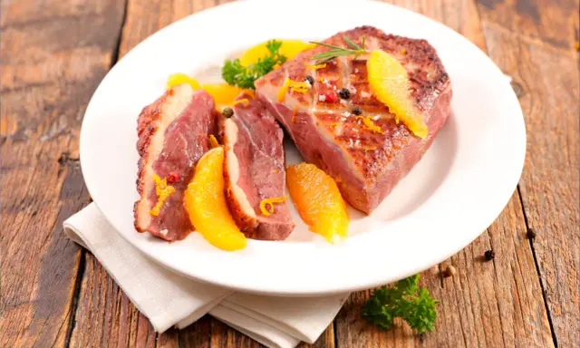 Magret de canard tranché, garni d'orange et de romarin, prêt à être dégusté. Une excellente recette plancha pour un repas savoureux.