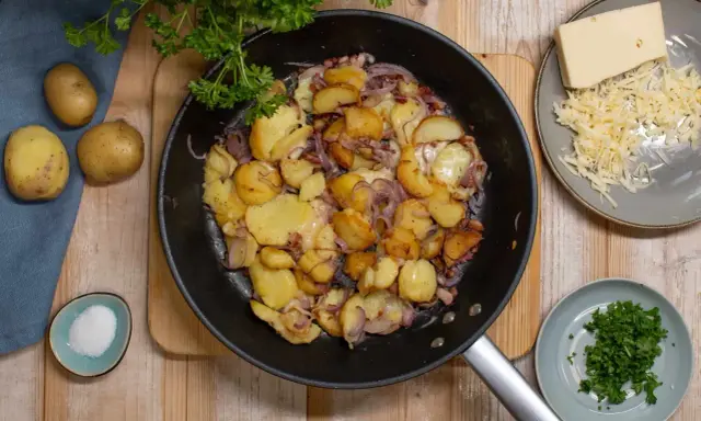Bratkartoffeln rezept: goldbraune Kartoffeln mit Zwiebeln und Käse in der Pfanne, dazu frische Petersilie und Salz.