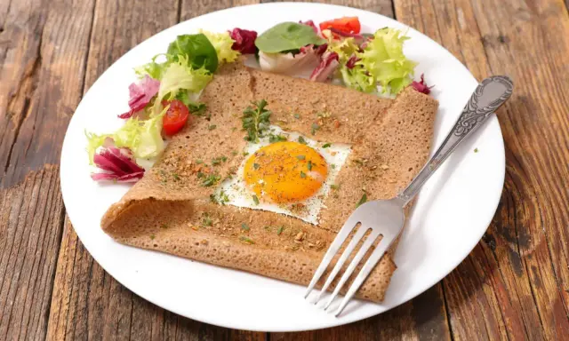 Galette bretonne complète au four, garnie d'un œuf au plat, d'herbes et servie avec une salade fraîche.