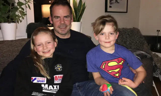 Marcus Oscarsson med sin familj, dottern och sonen sitter glatt i soffan.