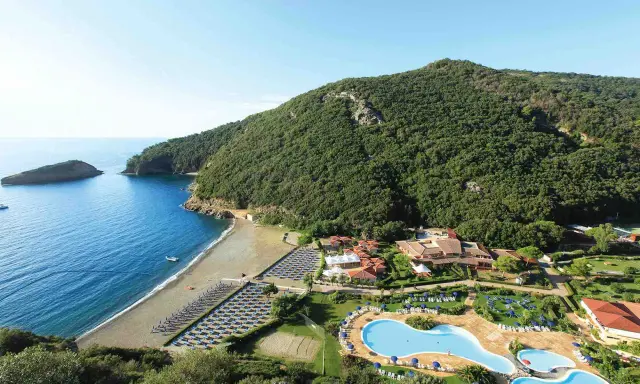 Villaggio toscana sul mare con spiaggia attrezzata, piscine e rigogliosa vegetazione che abbraccia la costa.
