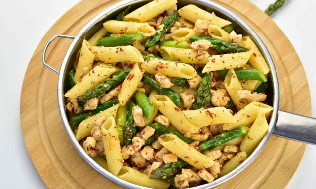 Penne z kurczakiem i szparagami, posypane płatkami chili. Pyszne danie na szybki obiad.