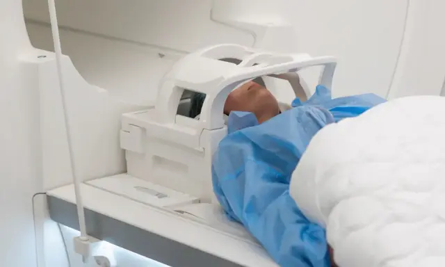 Pacjent w niebieskim fartuchu leży w aparacie MRI, przygotowany do badania głowy. Może to być związane z podejrzeniem nieprawidłowego rezonansu głowy.
