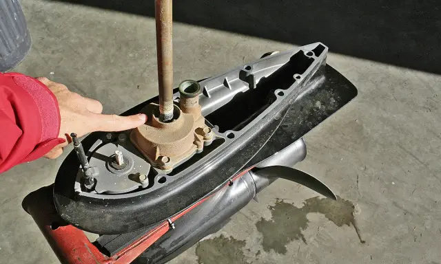 Main d'une personne en veste rouge pointant vers la turbine d'un moteur hors-bord Yamaha 2 temps, prêt à changer la pièce.