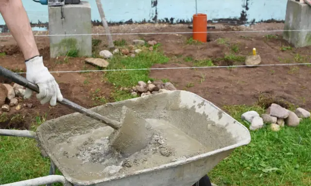 Hombre con guantes mezclando hormigón fresco en carretilla, parte de la puesta en obra del hormigón.