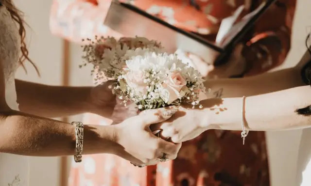 Manos entrelazadas sosteniendo un ramo de flores, un momento íntimo de los rituales boda civil.