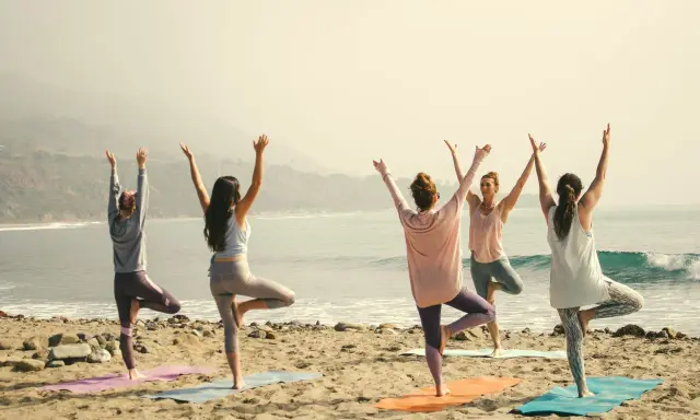 Kvinnor i trädposition på stranden. En lugn morgon för yoga, kanske en paus från pilates.