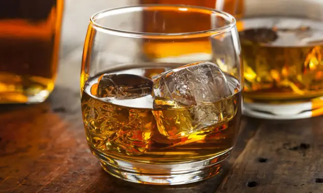 Szklanka złocistego trunku z lodem, otoczona butelkami. Czy to whisky szkocka czy irlandzka? Trudno zgadnąć, ale wygląda pysznie.