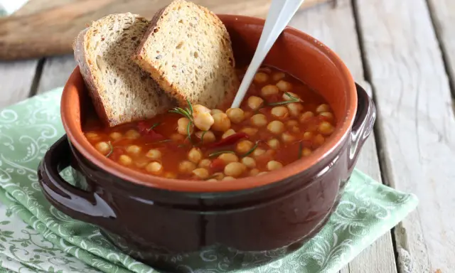Una ciotola di terracotta con zuppa di ceci, pomodoro e rosmarino, accompagnata da fette di pane rustico.