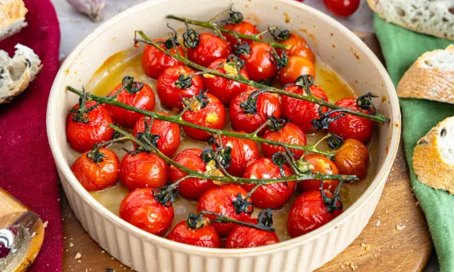 Konfierte Tomaten in einer Auflaufform, mit Brot und Knoblauch daneben.