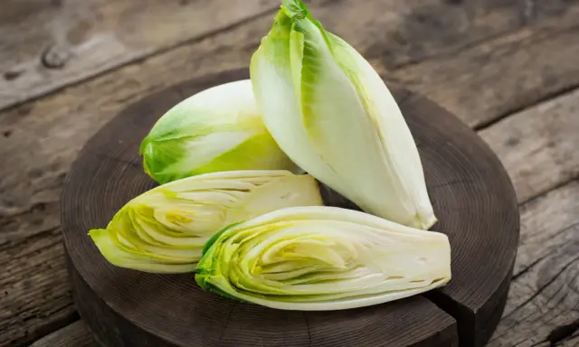 Frische Chicorée-Köpfe, einer davon halbiert, liegen auf einem Holzbrett. Perfekt für einen knackigen Chicorée-Salat.