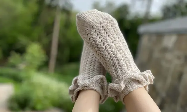 Piernas con calcetines de crochet color crema, con volantes en los tobillos y un delicado patrón calado.