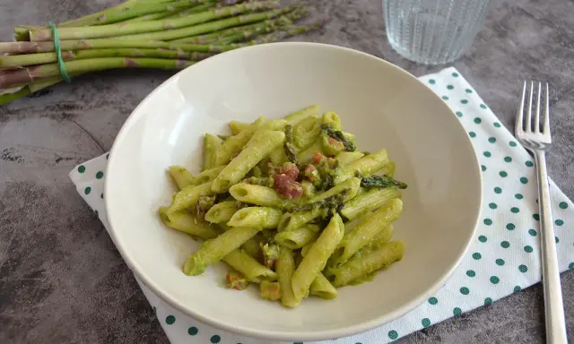 Penne cremose con asparagi freschi e cubetti di speck croccante, un piatto primaverile gustoso.