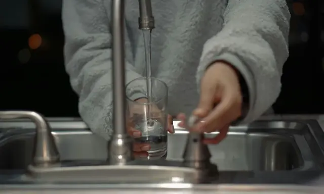 Mano llenando un vaso con agua del grifo, un problema común con el agua dura en España.