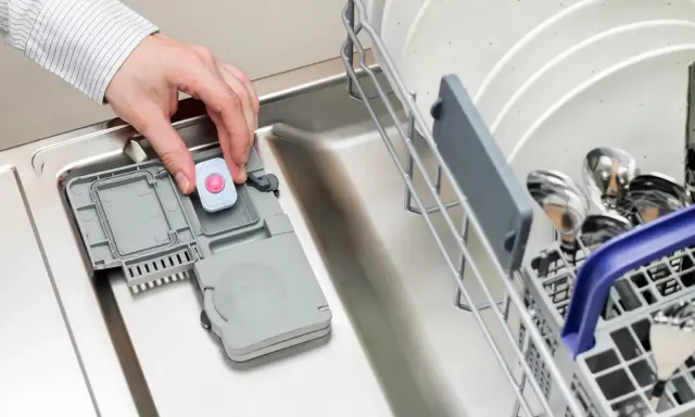 Dłoń wkłada tabletkę do zmywarki. Może to być rozwiązanie problemu, gdy zmywarka nie domywa górnego kosza.