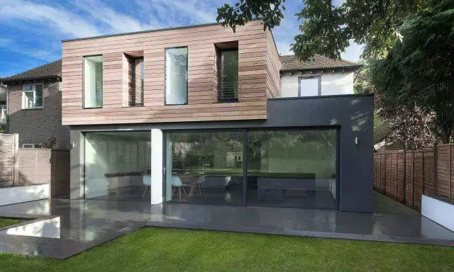 Une extension moderne en bois et anthracite pour agrandir une maison, avec de grandes baies vitrées donnant sur un jardin.