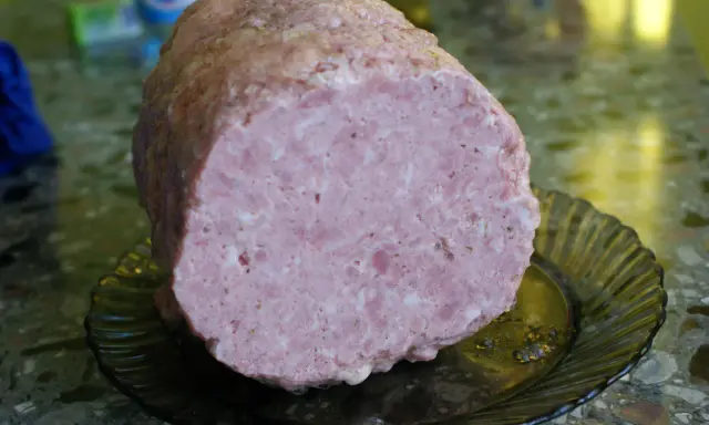 Pokrojona mielonka z szynkowara, różowa i soczysta, leży na ciemnej, karbowanej paterze.