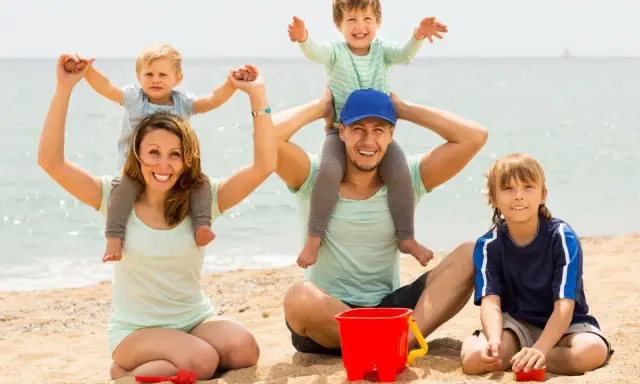 Famiglia felice in spiaggia, un modo perfetto per imparare come abbronzarsi in sicurezza mentre i bambini giocano con secchiello e palette.