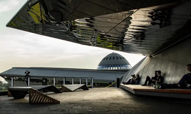 Nowoczesna architektura i ludzie odpoczywający pod zadaszeniem. W tle kopuła Muzeum Śląskiego, jedna z głównych katowice atrakcje.