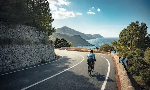 Rennradfahrer auf einer kurvigen Straße mit Blick auf das Meer und die Berge auf Mallorca.