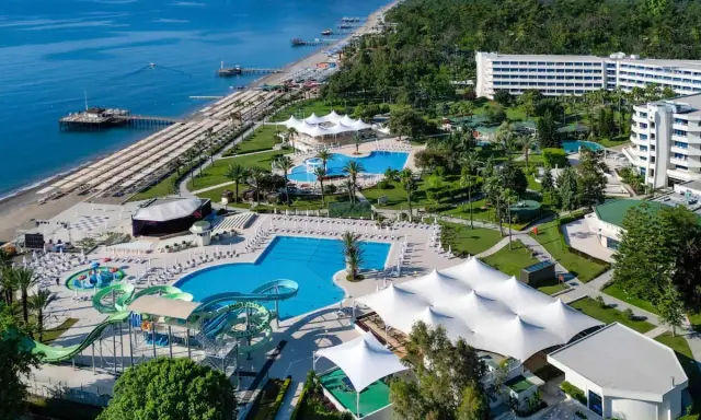 Widok z lotu ptaka na Mirage Park Resort: plaża, baseny, zjeżdżalnie wodne, białe pawilony i hotele otoczone zielenią.