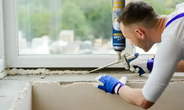 Mężczyzna w rękawiczkach nakłada piankę montażową na parapet. Czas, ile schnie pianka montażowa, zależy od warunków.