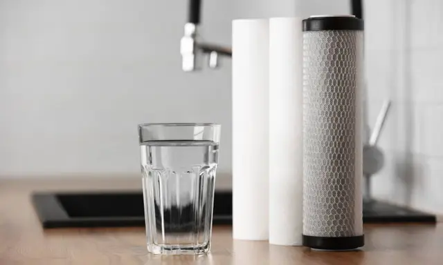 Verre d'eau pure à côté de cartouches filtrantes. Une solution pour la dureté de l'eau à Rouen.