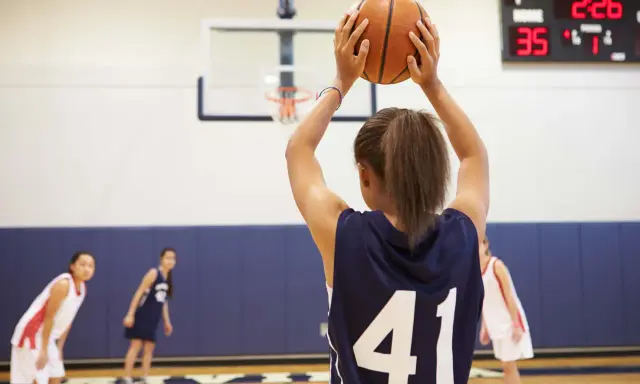 Ragazza con palla da basket, un ottimo sport per bambini iperattivi. In campo, altre giocatrici si preparano.
