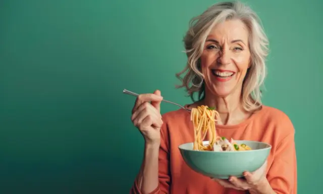 Uśmiechnięta seniorka zajada spaghetti. Pyszne danie, które pobudza co na apetyt dla seniora.