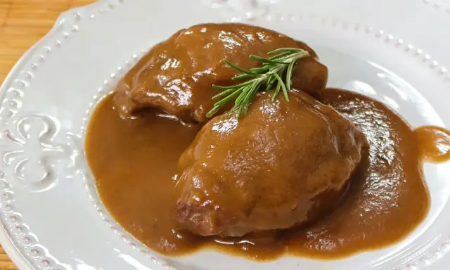 Deliciosas carrilleras de cerdo estofadas en salsa, coronadas con una ramita de romero fresco.