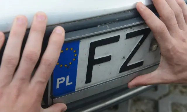 Dłonie trzymają tablicę rejestracyjną z oznaczeniem FZ.