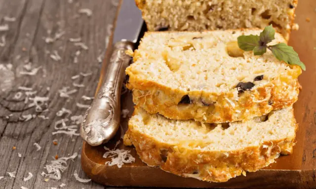 Pokrojona babka z cukinii z ziołami i serem, ułożona na desce, obok nóż.