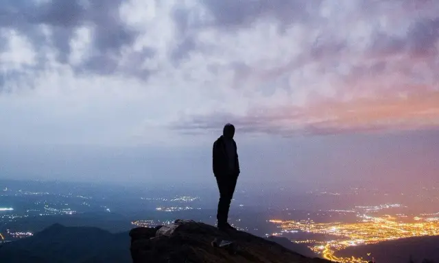 Silhouette di una persona su una rupe, con una città illuminata in lontananza. Un momento che fa amarcord, pensando a chi siamo e dove andiamo.