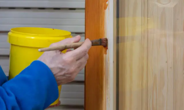 Persona aplica barniz a puerta de madera con brocha. Aprende como pintar puertas de madera para un acabado perfecto.