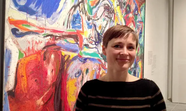 Kvinna ler framför en färgstark målning i Asger Jorns stil.