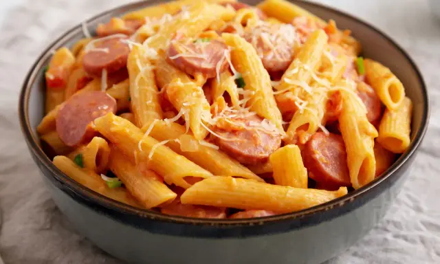 Penne z sosem pomidorowym i plasterkami kiełbasy, posypane startym parmezanem. Pyszne danie makaron z kiełbasą.