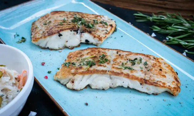 Zwei perfekt gegrillte Kabeljaufilets, mit Kräutern bestreut, serviert auf einem blauen Teller. Genießen Sie kabeljau grillen ohne alufolie!