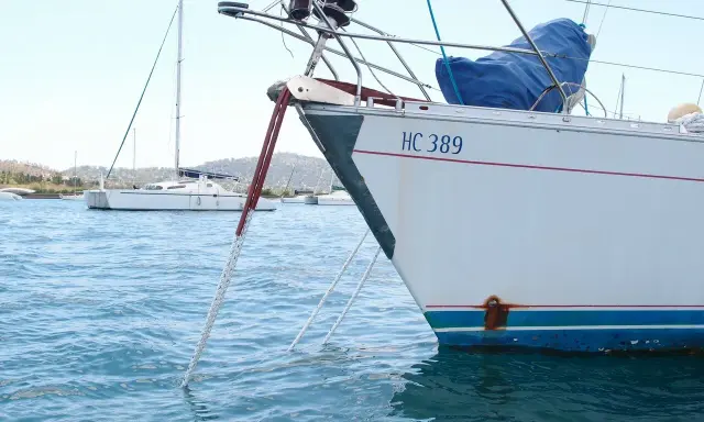 Poids corps mort pour bateau : une ancre est immergée dans l'eau bleue, attachée à un voilier blanc immatriculé HC 389.